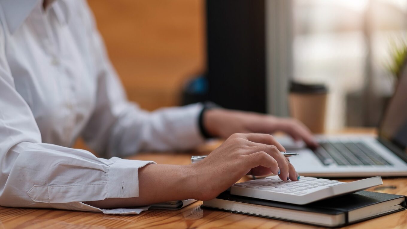 Close up Business woman using calculator and laptop for do math finance on wooden desk in office and