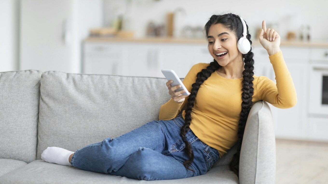 Cheerful Young Indian Woman Browsing Music Streaming Services On Smartphone At Home
