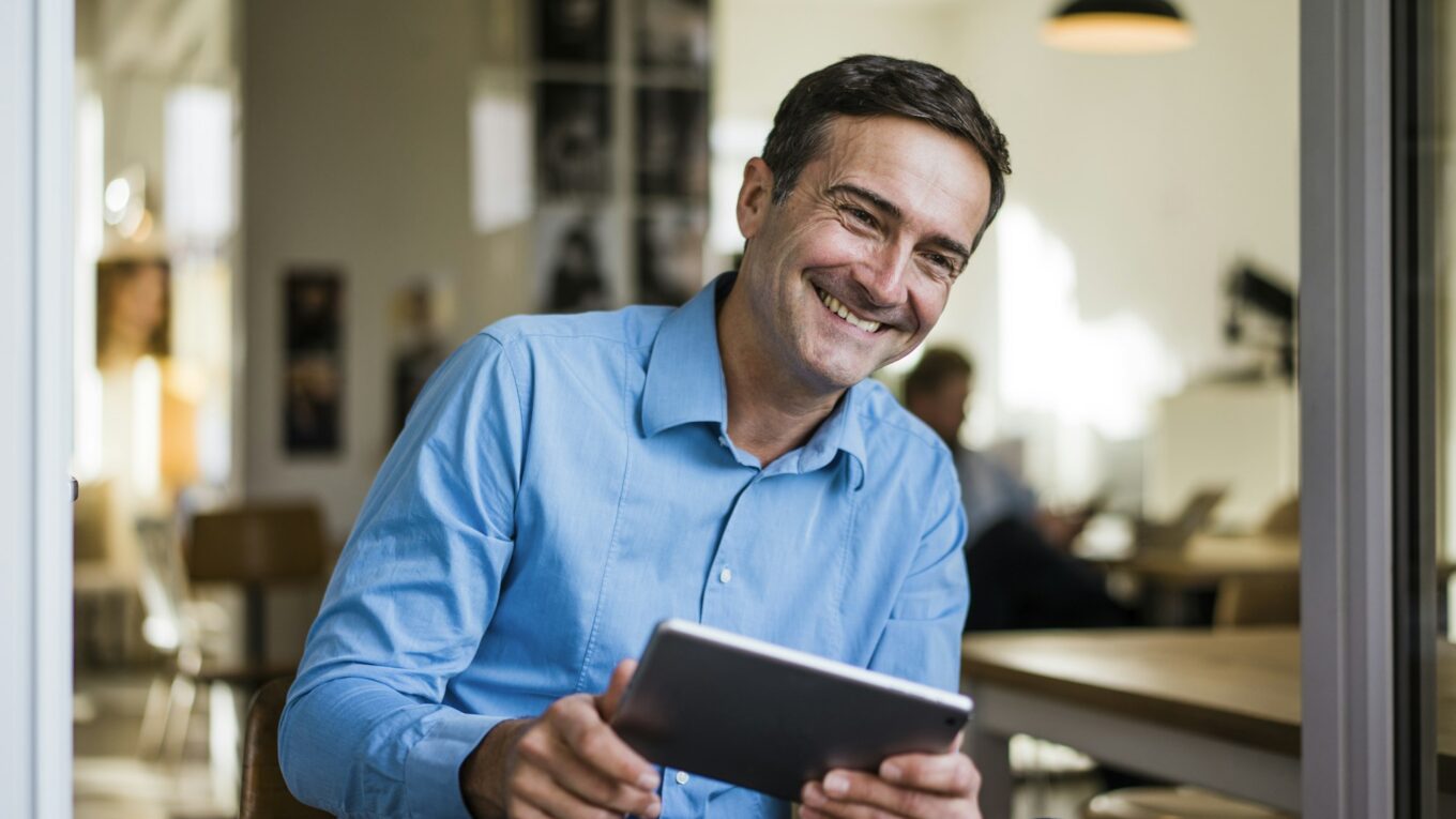 Smiling businessman with tablet sitting at open French door